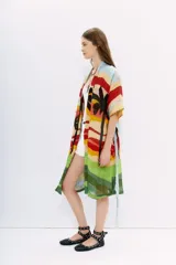 Kimono largo de lino con estampado vibrante que simula un paisaje de atardecer con palmeras, en franjas horizontales de colores cálidos y verdes. Posee mangas amplias y lazo para ajustar en la cintura.