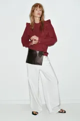 Blusa de manga larga con cuello redondo, volantes en los hombros y detalle de jaretas frontales. Presenta bordados perforados en toda la prenda y cierre posterior con botones ocultos.