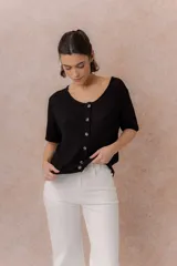 Cardigan tejido de manga corta color beige, con escote redondo amplio y abotonadura frontal con botones al tono. Presenta un calce relajado y terminaciones en rib en la cartera y el ruedo.