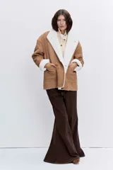 Cazadora de efecto piel en color tostado con interior y solapas de borreguillo blanco. Presenta cierre frontal con botones, bolsillos laterales y mangas largas con puños de borreguillo.