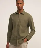 Camisa de corte regular color verde militar, con cuello camisero, mangas largas y dos bolsillos frontales con solapa y botones. Confeccionada en tejido plano de mezcla de poliéster y algodón.