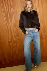 Jeans de tiro alto, color gris oscuro lavado, con pierna ancha extra larga (full length) y diseño de cintura cruzada asimétrica con cierre frontal de cremallera y botones metálicos.