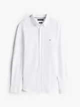 Camisa de manga larga Tommy Hilfiger confeccionada en tejido interlock, con corte slim, cuello clásico y cierre frontal de botones. Presenta el logo de la marca bordado en el pecho.