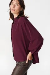 Camisa de pana color verde oliva, con cuello mao, cierre frontal de botones y mangas largas abullonadas con puños elásticos.