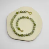 Collar de cuentas redondas de serpentina en tonos de verde claro y blanco, ensartadas con hilo verde y terminaciones y broche tipo anilla de acero con baño de oro.