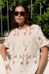 Blusa de encaje con diseño floral y geométrico translúcido, de manga corta y cuello redondo.