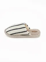 Pantuflas abiertas de estilo mule, con capellada de peluche color crema con rayas negras horizontales y plantilla de pana acanalada en tono beige.