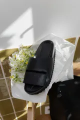 Sandalias tipo chinelas color negro con suela anatómica y diseño de banda ancha con abertura horizontal.