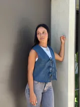 Chaleco de jean azul con cierre frontal mediante lazos ajustables, sin mangas y corte recto.