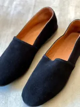 Mocasines de silueta clásica confeccionados en gamuza negra, con punta redondeada, diseño de calce simple y suela baja.