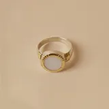 Anillo de diseño circular con centro de nácar y borde texturizado en tono dorado, montado sobre una banda de plata.