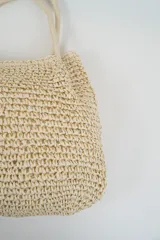 Bolso tipo tote de tejido de punto en color beige, con diseño de textura trenzada y asas largas de cuerda.