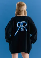 Buzo oversize de cuello redondo, confeccionado en frisa esmerilada color negro. Presenta hombros caídos y una estampa grande en la espalda con el logo de la marca en azul con diseño de rayas tipo animal print.