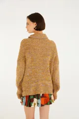 Sweater tejido color mostaza con cuello alto, mangas largas y un gran bordado floral en el frente con detalles colgantes.