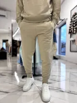 Conjunto de jogging beige que incluye un hoodie con capucha, bolsillo frontal tipo canguro y pequeño texto estampado en el pecho, acompañado de un pantalón tipo jogger con elástico en los tobillos.