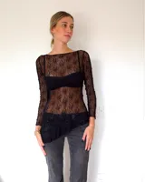 Vestido corto de encaje negro con diseño asimétrico en el ruedo. Presenta mangas largas y un corte ajustado, con un estilo que combina transparencia y texturas.