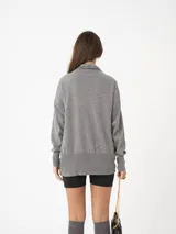 Sweater gris de tejido fino con cuello alto, silueta amplia y hombro caído.