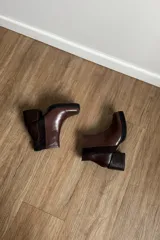 Botines de cuero vacuno en color marrón, con diseño de caña media, taco cuadrado y plataforma delantera. Presentan una combinación de texturas en el cuero y un estilo robusto.