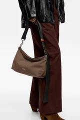 Bolso bandolera de tamaño mediano confeccionado en nylon negro, con estructura blanda, asa regulable de tejido, logo metálico de la marca en el frente y cierre con cremallera.