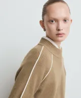 Sweater de punto color beige, con cuello alto y diseño de manga larga raglán con detalle de línea blanca lateral. Presenta un tejido acanalado y corte recto.