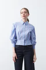 Camisa a rayas azules y blancas de manga larga, con cuello clásico y puños abotonados. Presenta un diseño entallado en la cintura.