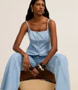 Chaleco largo de jean con escote recto, breteles finos ajustables y cierre frontal con botones. Presenta un corte acinturado con pences, bolsillos delanteros decorativos y ruedo en punta.