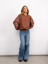 Campera de jogging negra con cierre frontal, cuello con detalle de volados y bordados florales en las mangas. Presenta un corte holgado y puños elásticos.