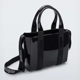Cartera tipo tote bag Melissa modelo Mini Dulce, color negro brillante, fabricada en Melflex (PVC flexible y vegano). Cuenta con doble asa de mano y una correa ajustable y removible con el nombre de la marca estampado.