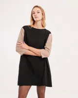 Vestido corto negro con mangas 3/4 verdes, cuello bote y bolsillos laterales.