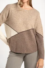 Sweater de tejido de punto con diseño color block en tonos beige, crema y marrón, separados por costuras en hilo marrón oscuro. Presenta cuello redondo y calce al cuerpo.