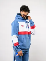 Canguro con capucha de Umbro del Club Nacional de Football, con diseño de bloques de color en azul, blanco y rojo. Presenta bolsillo frontal tipo canguro, cordones ajustables en la capucha y logos bordados del club y la marca.