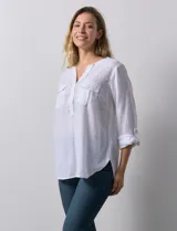 Blusa blanca de lino y rayón, con cuello a la base, escote en V y abertura con botones. Tiene bolsillos en la parte delantera y mangas largas regulables con presilla y botón.