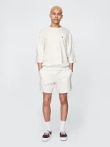 Remera de corte oversized en color beige claro, con cuello redondo y mangas de largo medio. Presenta un pequeño bordado del oso Brannan de Gap en el lado izquierdo del pecho.