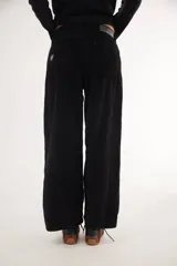 Pantalón de pana de corte ancho y tiro medio-bajo, con diseño de cinco bolsillos y acabado lavado. Presenta un aplique cuadrado decorativo en una de las piernas y un pin bordado de la marca.