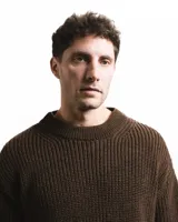 Buzo unisex de tejido de punto grueso en lana merino, color rojo, con cuello redondo y diseño de calce relajado. Presenta un detalle bordado a mano en contraste en la manga.