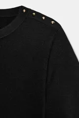 Jersey negro de punto de manga corta y cuello redondo, con detalle de botones dorados en el hombro.