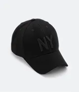 Gorra de seis paneles con ala curva, confeccionada en algodón color marrón. Presenta un bordado frontal con las letras NY en color blanco y cuenta con cierre strapback ajustable en la parte posterior.
