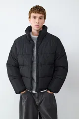 Campera acolchada de color negro con cuello alto, cierre frontal de cremallera y diseño de paneles horizontales. Cuenta con mangas largas y bolsillos laterales funcionales.
