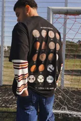 Remera oversize de algodón color negro, con diseño gráfico en la espalda que presenta una serie de pelotas de fútbol históricas y el texto 'Uruguayos Campeones de América y del Mundo'.