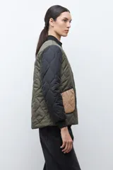 Campera bomber reversible con diseño capitoneado, cuerpo en color verde oliva y mangas negras. Presenta cierre frontal, cuello, puños y ruedo acanalados, y un bolsillo de parche en color beige.