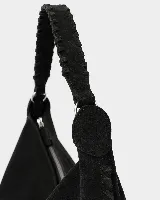 Bolso tipo hobo de gran tamaño, confeccionado en gamuza negra con detalles de costuras artesanales y tientos decorativos en los bordes. Cuenta con un asa trenzada con pespuntes a mano y cierre superior.
