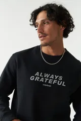 Buzo negro de felpa con cuello redondo y lettering estampado en el frente con la frase 'Always Grateful' y la marca 'Mistral'.