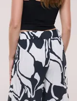 Pantalón ancho negro y blanco con estampado abstracto, cintura elástica con cordón ajustable, bolsillos delanteros con detalles de pompones y corte tobillero.