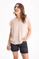 Blusa de manga corta color beige, confeccionada en tela crepé, con escote en V y sutil fruncido en el pecho.