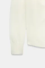 Jersey de punto fluido color blanco, con cuello redondo, manga larga y detalle de pliegues drapeados en el hombro.