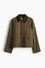 Campera de sarga color verde militar, con cuello camisero de pana marrón oscuro, cierre frontal con solapa y botones a presión metálicos, bolsillos frontales grandes con solapa y mangas raglán.