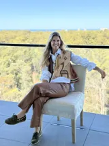 Chaleco tejido de punto con diseño asimétrico, presentando un lado en color marrón oscuro y otro en beige, ambos decorados con motivos geométricos y figuras de llamas bordadas. Posee cierre frontal con cordones de cuero y terminaciones en tejido elástico con franjas decorativas.