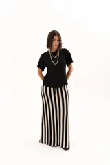 Pollera larga de tejido de punto con diseño de rayas verticales en color negro y crudo. Presenta una pretina elástica con cordón de ajuste y tajos laterales profundos que aportan movimiento.