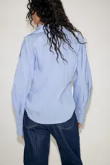 Camisa de manga larga con cuello solapa y escote en pico. Presenta un diseño entallado en la cintura y cierre frontal mediante botones.
