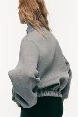 Buzo de corte holgado en tejido con efecto neopreno, con hombros caídos, cuello elevado y tapeta frontal con botones a presión ocultos. Presenta puños y bajo con elástico revestido.